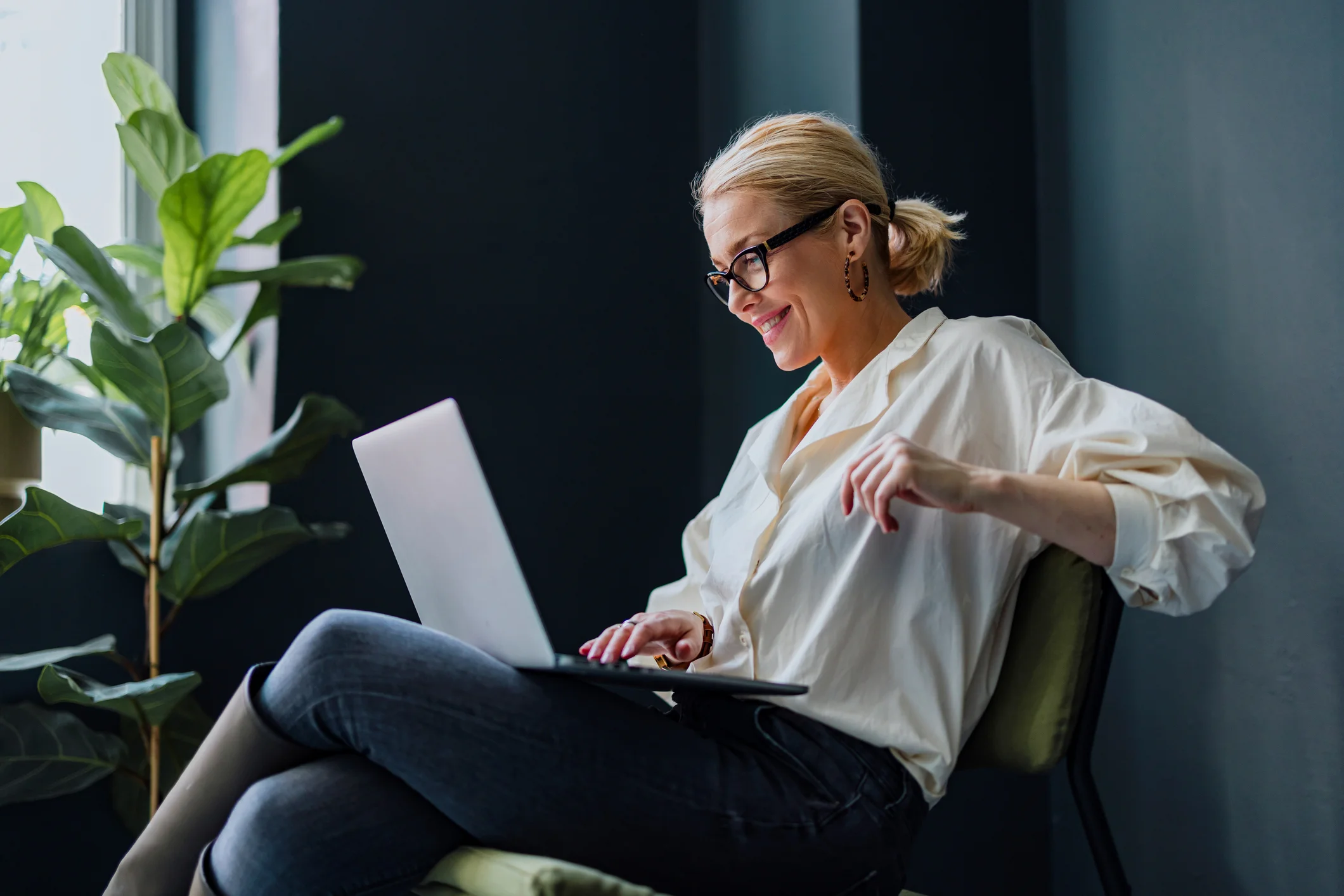 Cheerful smiling businesswoman sitting on a chair and typing business report on a laptop keyboard.